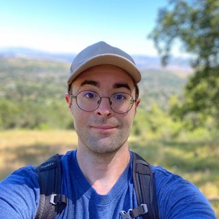 Ryle Goehausen on a hiking trail, wearing a cap and round glasses.